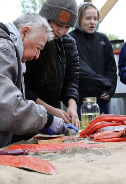 Mary Lou Bottorff shows young participants in a Yinihugheltani workshop in June how to strip and smoke salmon. The tribe's Yinihugheltani program is using activities for young people to build resilience and strengthen relationships with a longer term goal of lowering the peninsula's suicide rate.