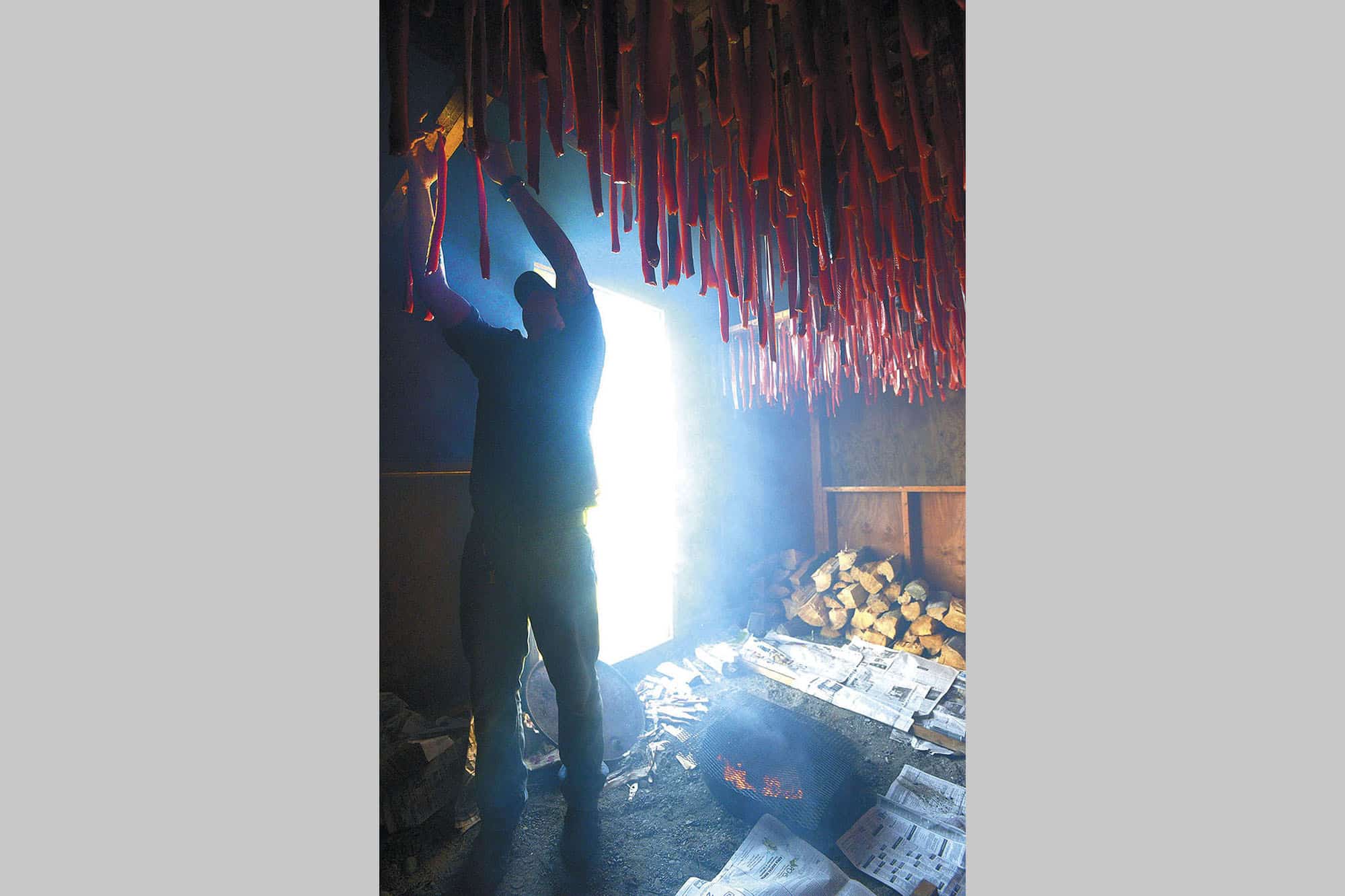Kaleb Franke hangs salmon strips in the smokehouse at the tribe’s waterfront fishery.